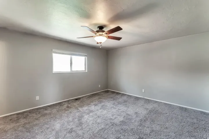 Spacious room featuring neutral gray walls, gray carpeting, and a ceiling fan with integrated lighting