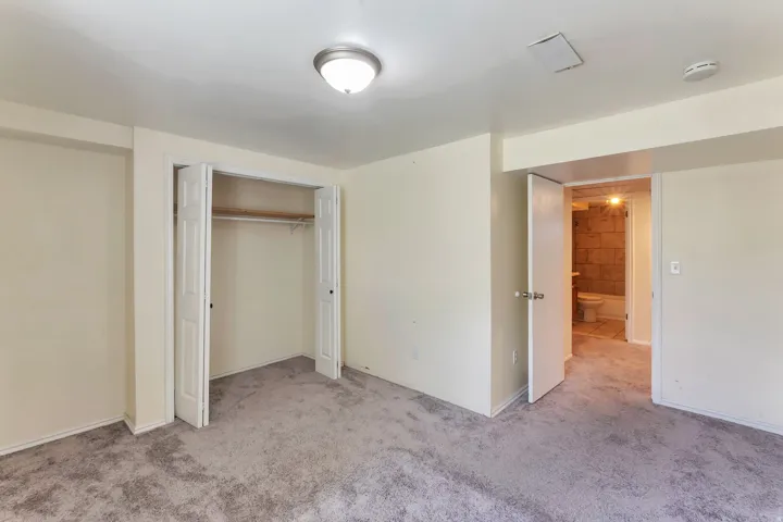 Carpeted room featuring a ceiling-mounted light fixture, bi-fold closet doors, and access to a bathroom with tile flooring and a tub-shower combination