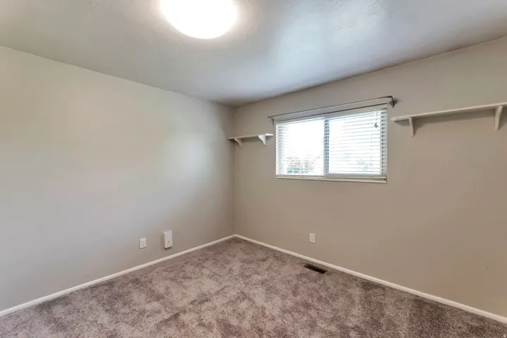 Carpeted room featuring neutral wall tones, a ceiling-mounted light fixture, white trim, and a window with blinds