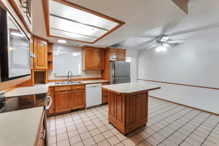 Kitchen featuring wood cabinetry, stainless steel appliances, a ceiling fan with light fixture, and a skylight