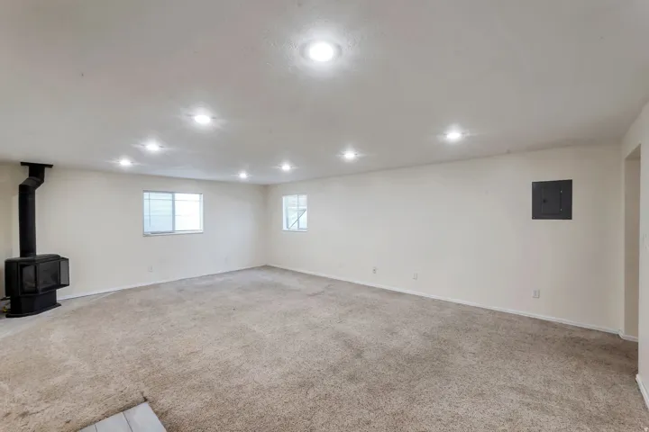 Spacious room featuring a freestanding black stove, recessed ceiling lighting, two windows with blinds, and neutral-toned carpeting
