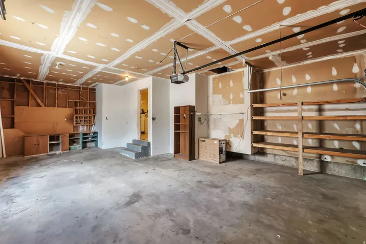 Spacious garage featuring a concrete floor, exposed ceiling joists, and a built-in wooden shelving unit