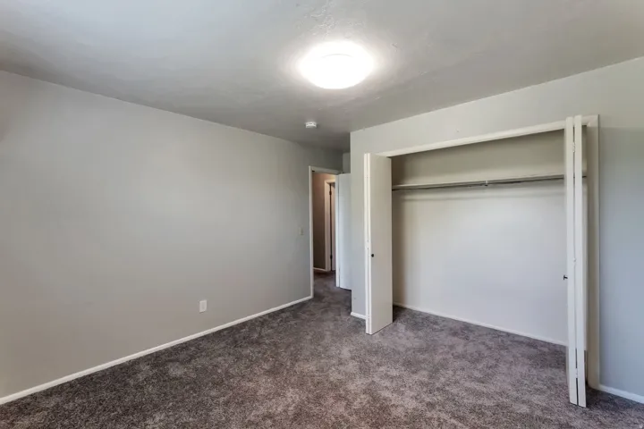 Bedroom with neutral gray walls, gray carpet, white baseboards, and a bi-fold closet with a hanging rod