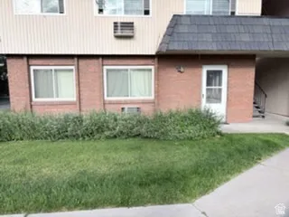 Ground-level unit featuring brick exterior, two windows, a white entry door, and a partially covered entryway