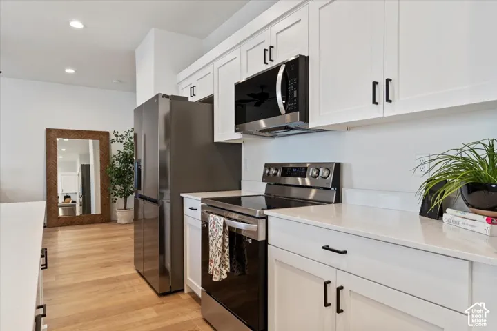 Modern kitchen featuring white shaker cabinetry, stainless steel appliances, light wood-finish flooring, and recessed lighting