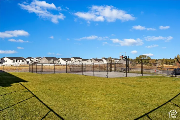 Lush green lawn bordering a fenced recreational area featuring a basketball court and a tennis court