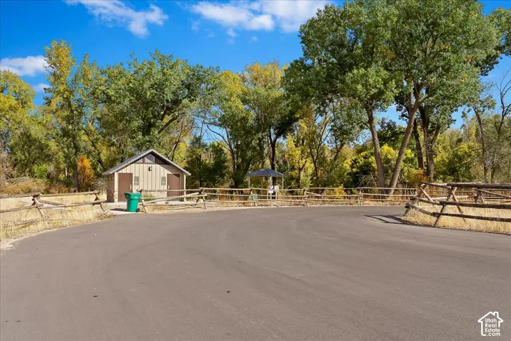 Asphalt paved area bordered by a split rail fence, featuring a small utility building with a pitched roof and a shaded gazebo structure