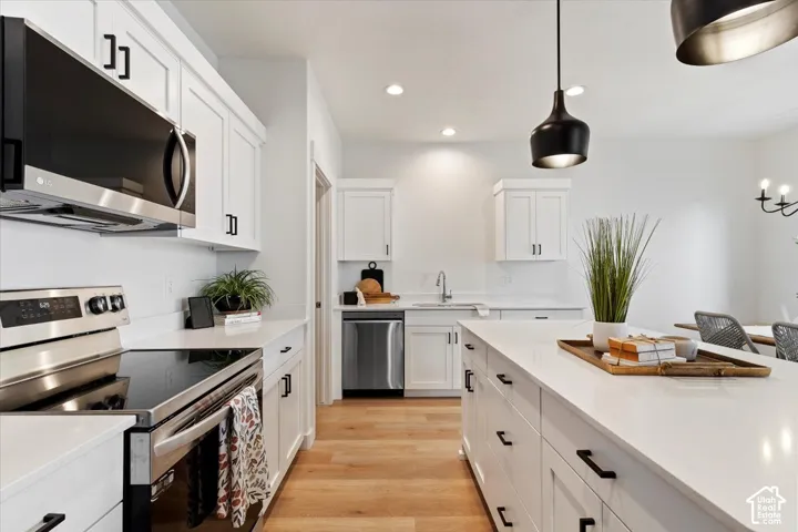 Modern kitchen featuring white shaker cabinetry, stainless steel appliances, a large center island with a white countertop, and light wood-finish flooring