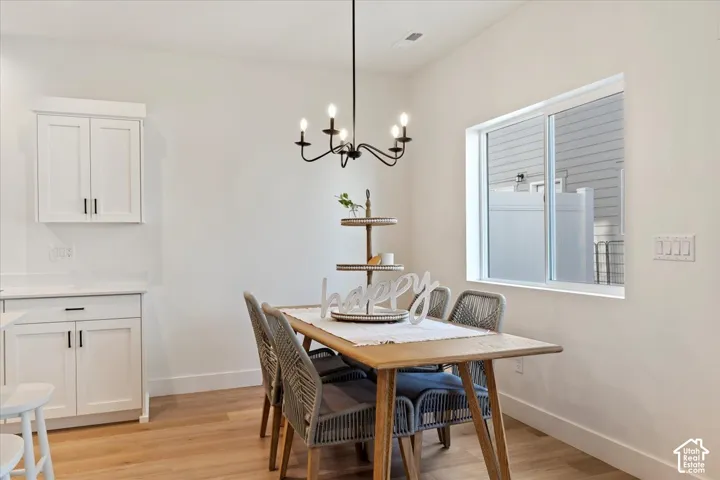 Dining area featuring wood-finish flooring, white walls, and a contemporary chandelier