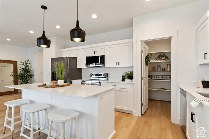 Modern kitchen featuring a large central island with a light-toned countertop, white cabinetry with dark hardware, stainless steel appliances, and wood-finish flooring