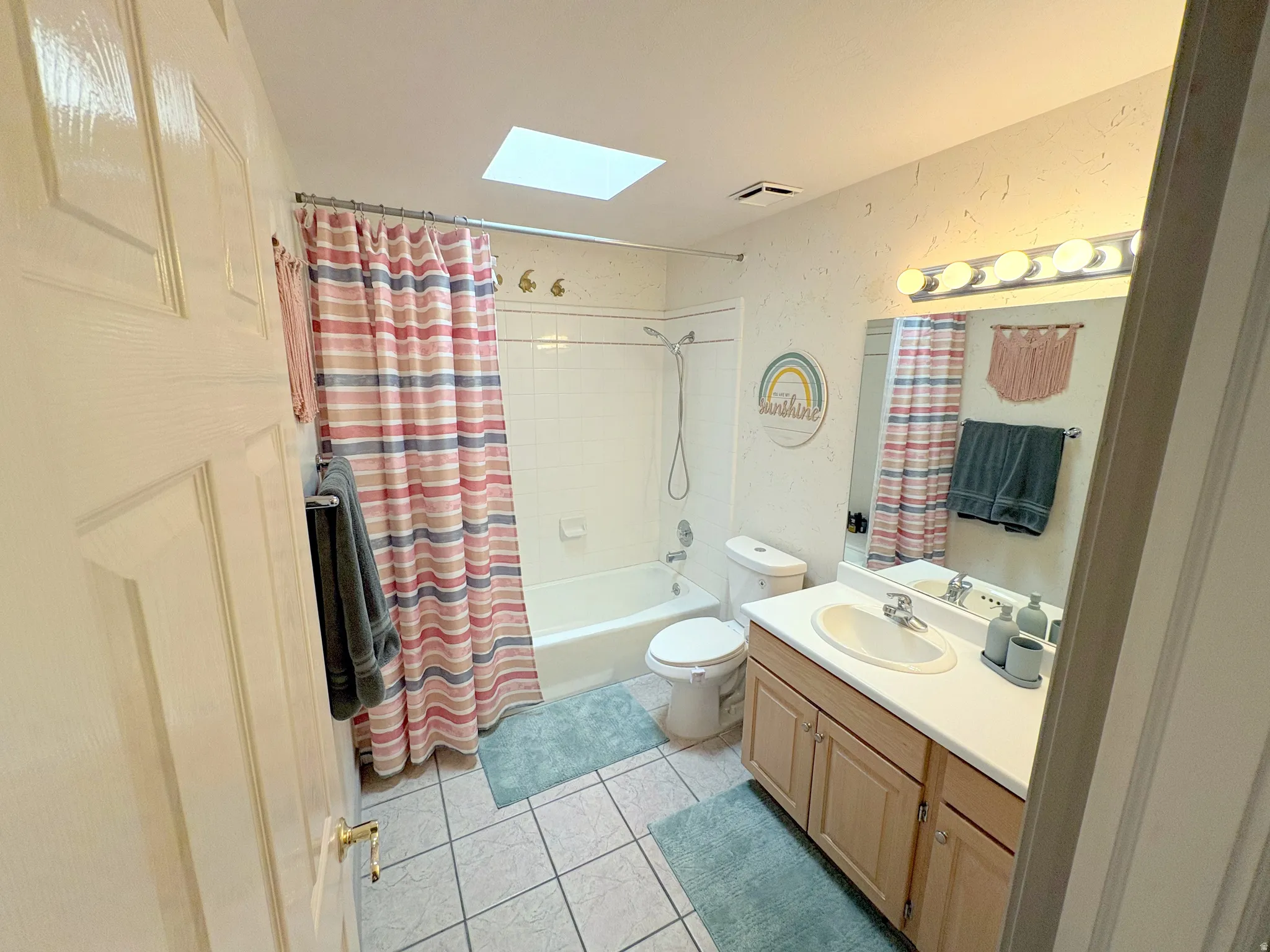 Bathroom featuring a skylight, a single vanity with wood-finish cabinetry, a white countertop, and an integrated sink