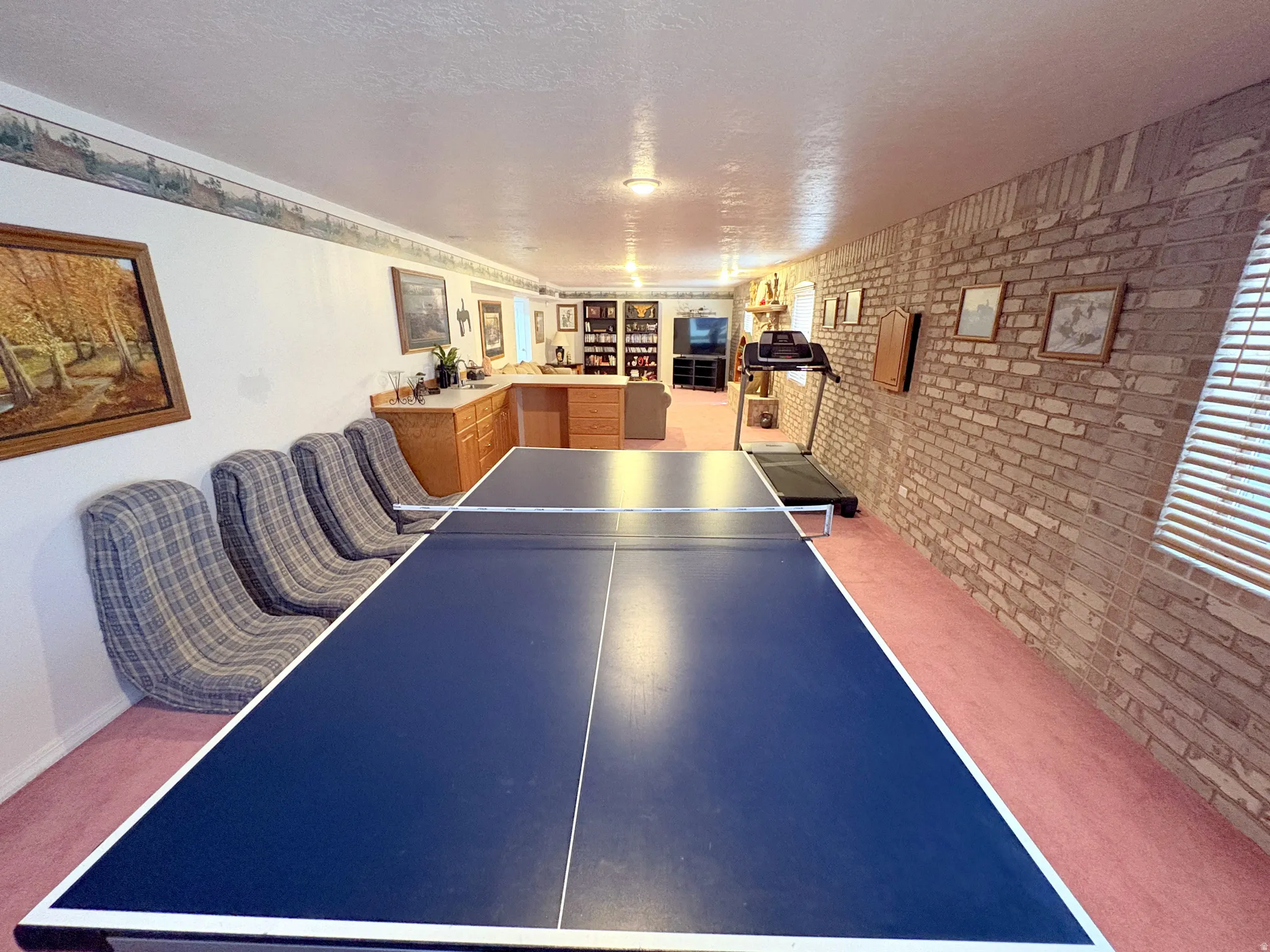 Expansive recreation space featuring a brick accent wall, recessed lighting, built-in cabinetry, and wall-to-wall carpeting
