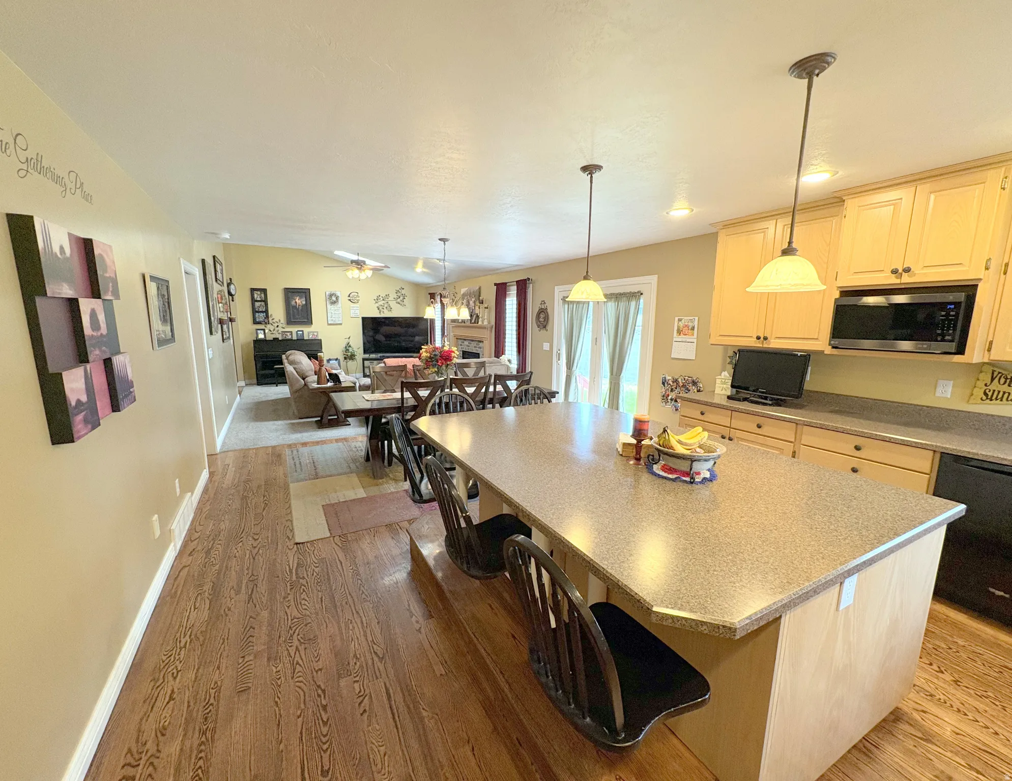 Open-concept kitchen featuring an expansive center island with seating, pendant lighting, wood-finish flooring, and light wood cabinetry with built-in microwave