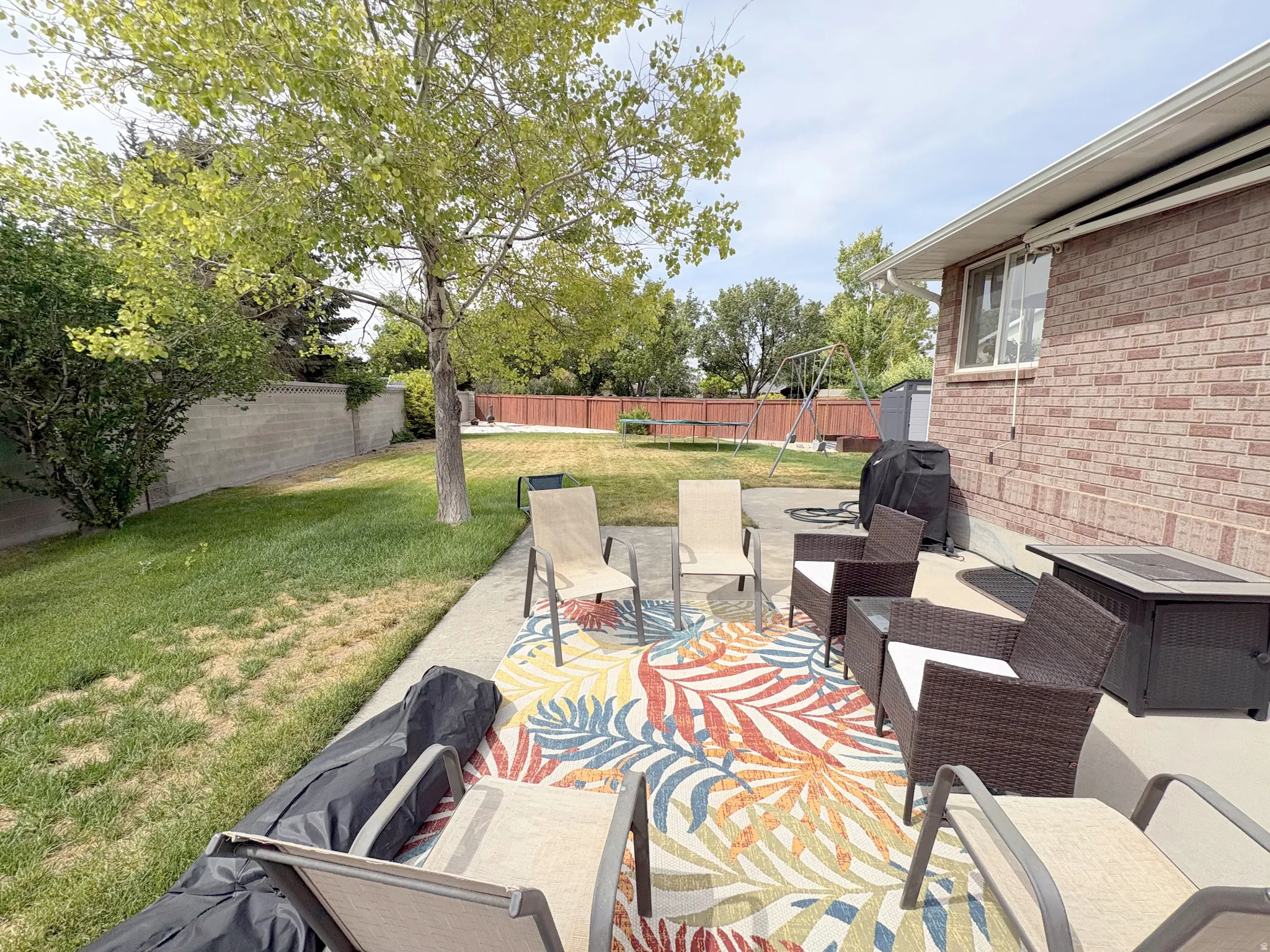 Expansive backyard featuring a concrete patio, a mature tree, and a brick exterior