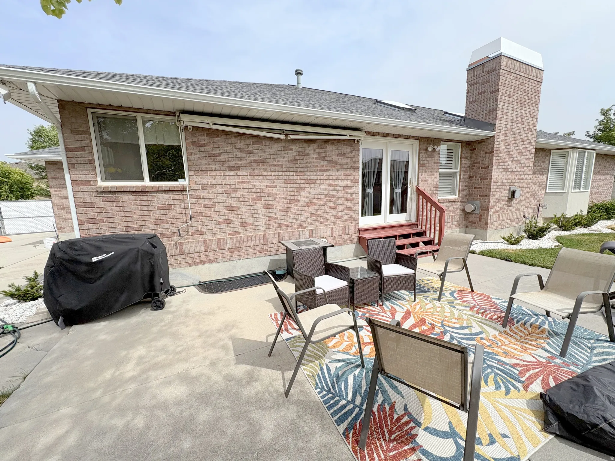 Expansive concrete patio area with a red brick exterior, a substantial brick chimney, and a double patio door with red-painted steps