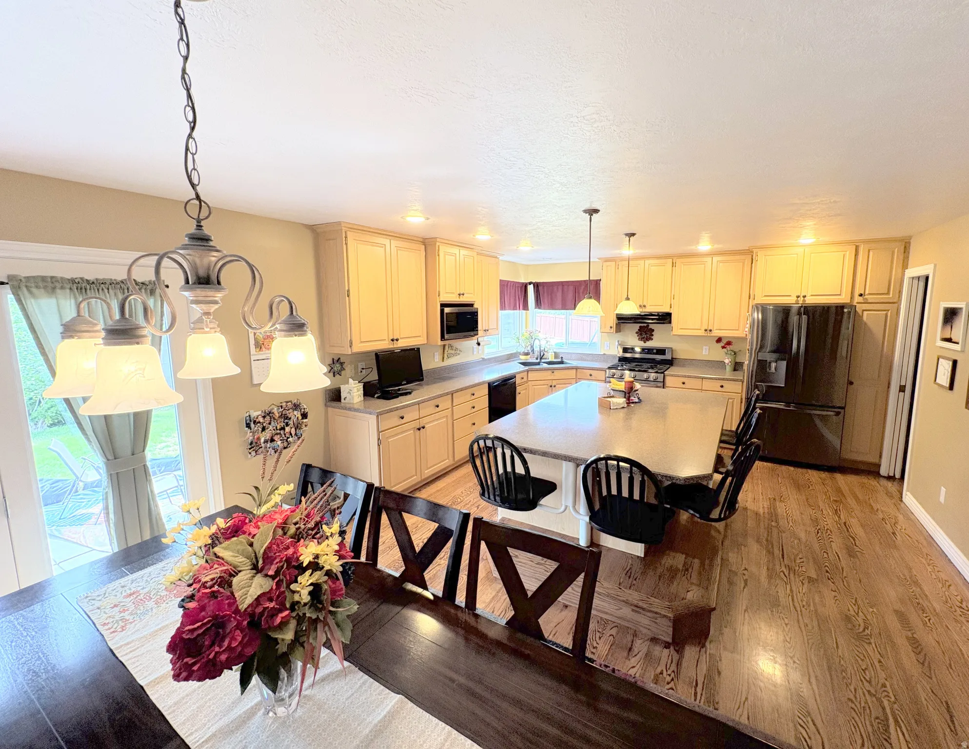 Open-concept kitchen featuring light-toned cabinetry, a large kitchen island with seating, stainless steel appliances, and wood-finish flooring