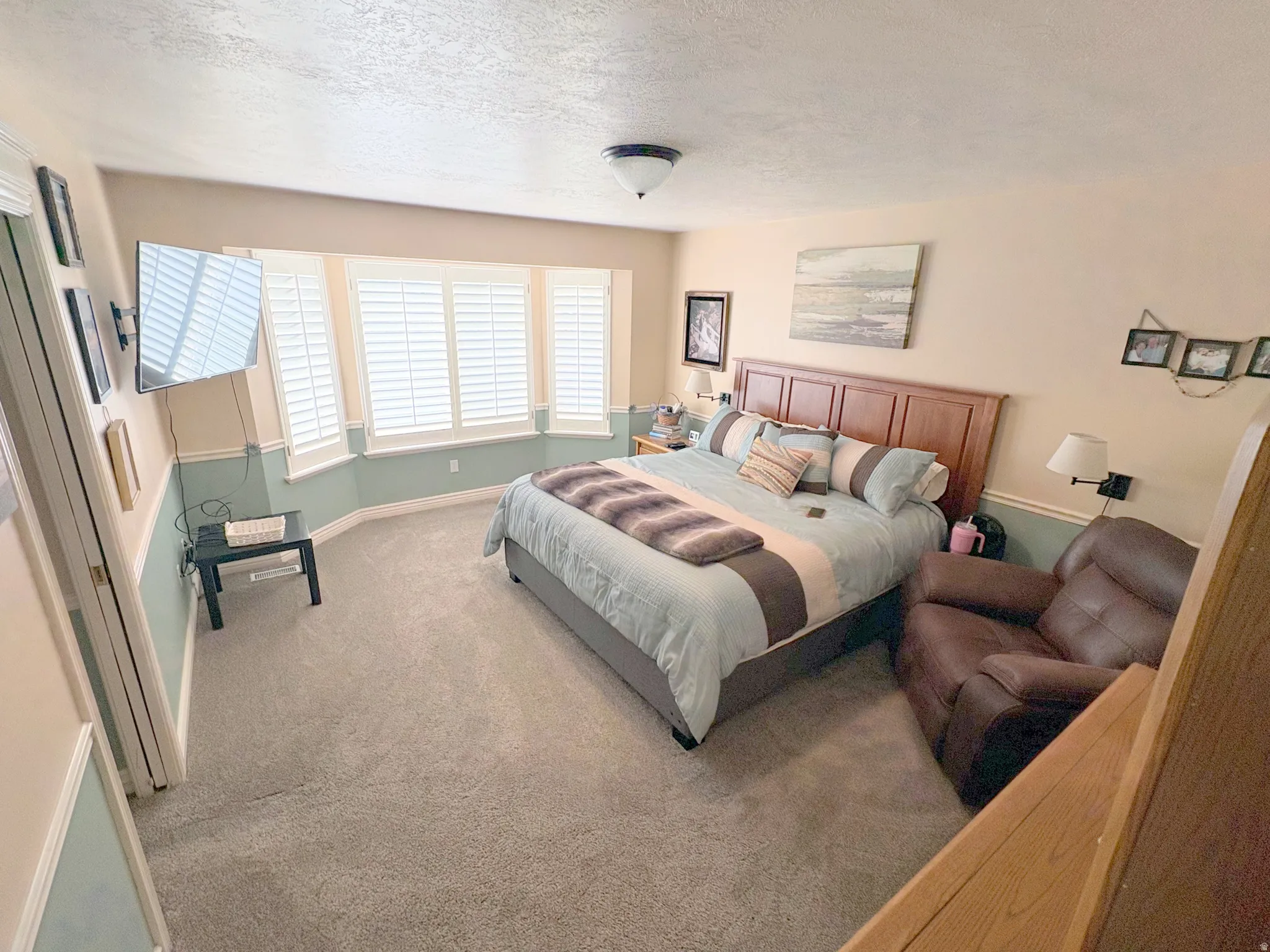 Spacious room featuring a bay window with plantation shutters, neutral carpeting, and a two-tone wall treatment