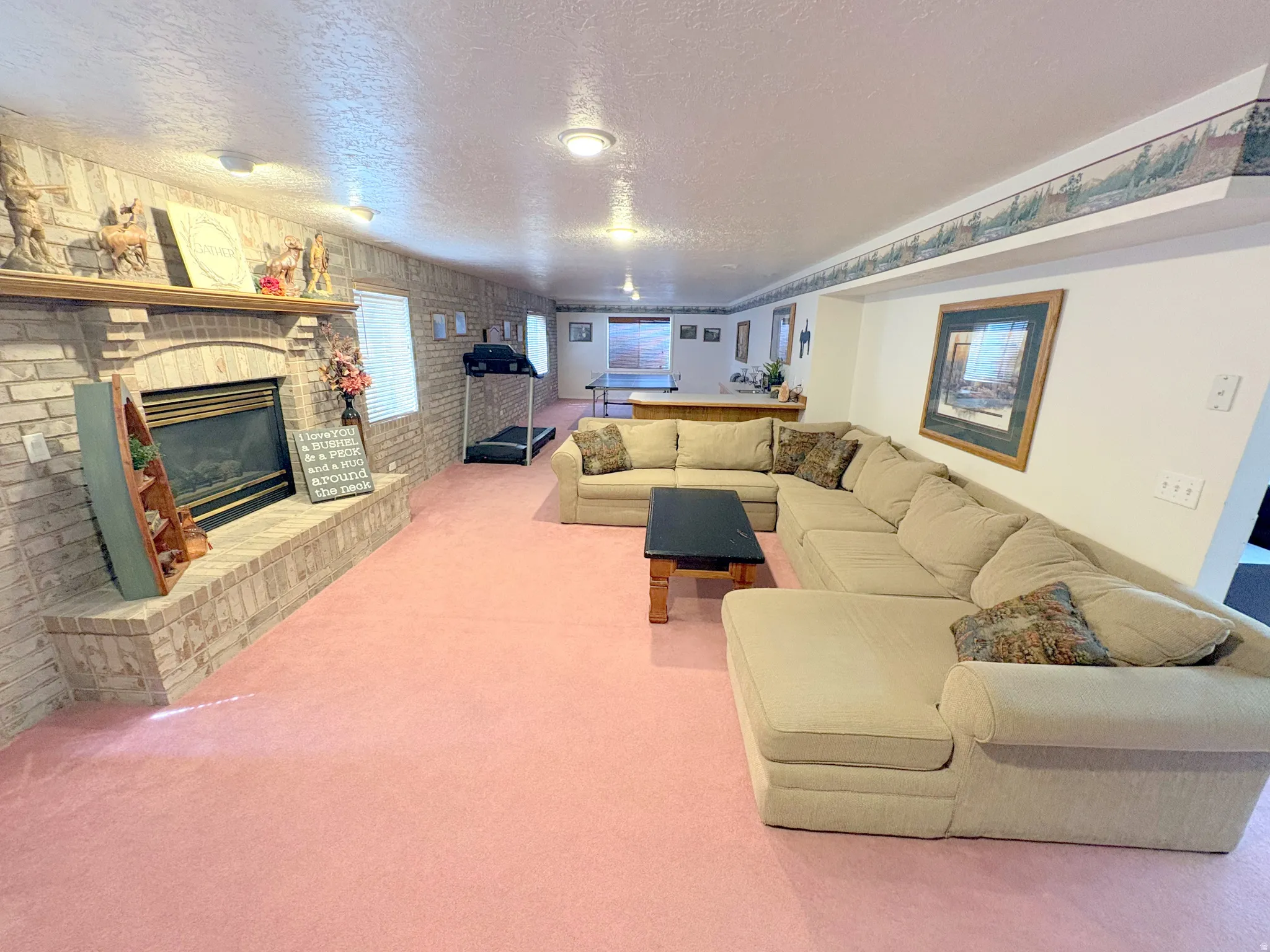 Spacious lower-level area featuring a brick-surround fireplace with a hearth and wood mantel