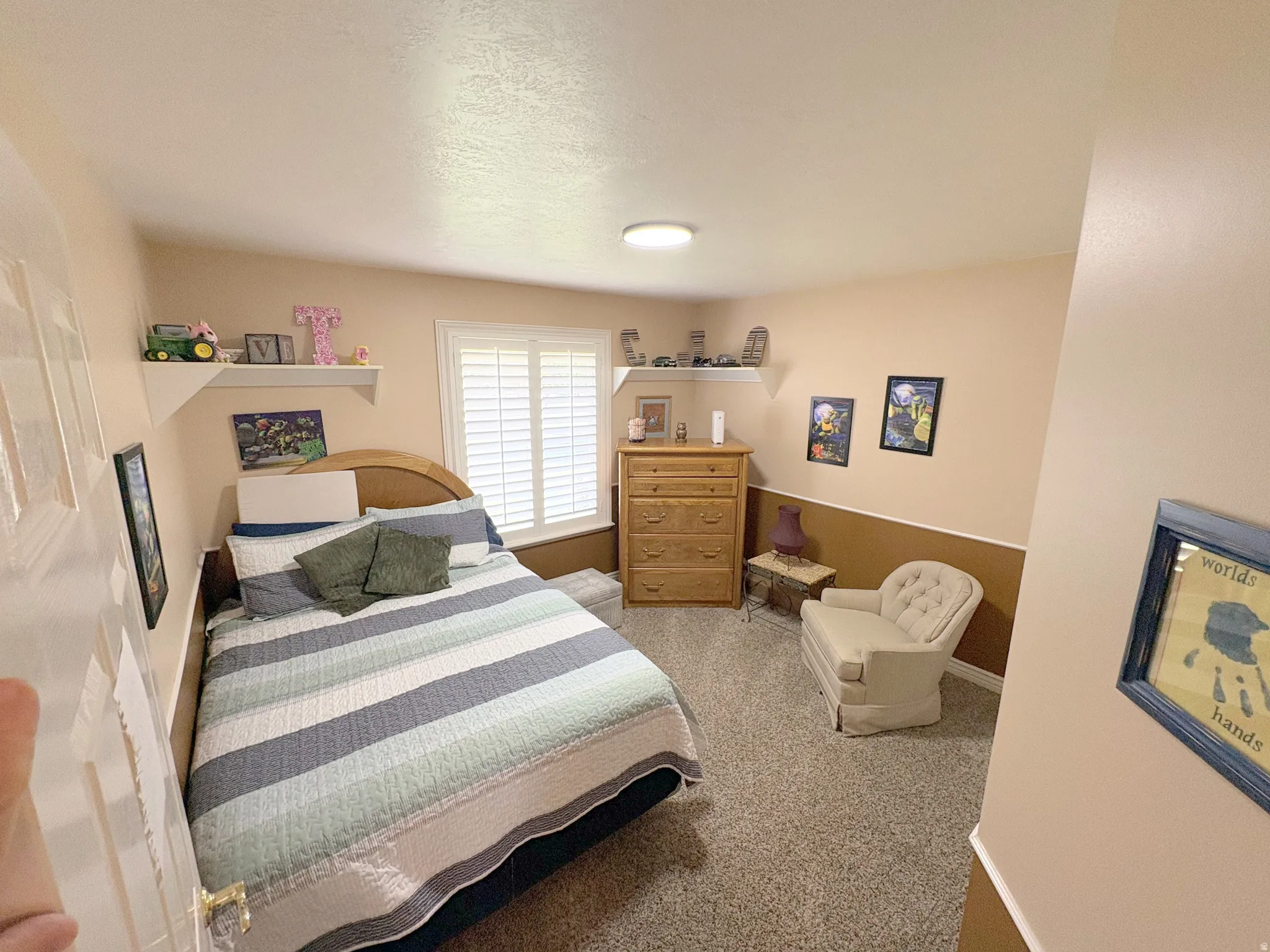 Carpeted room featuring a window with plantation shutters, two wall-mounted shelves, and a two-tone wall finish