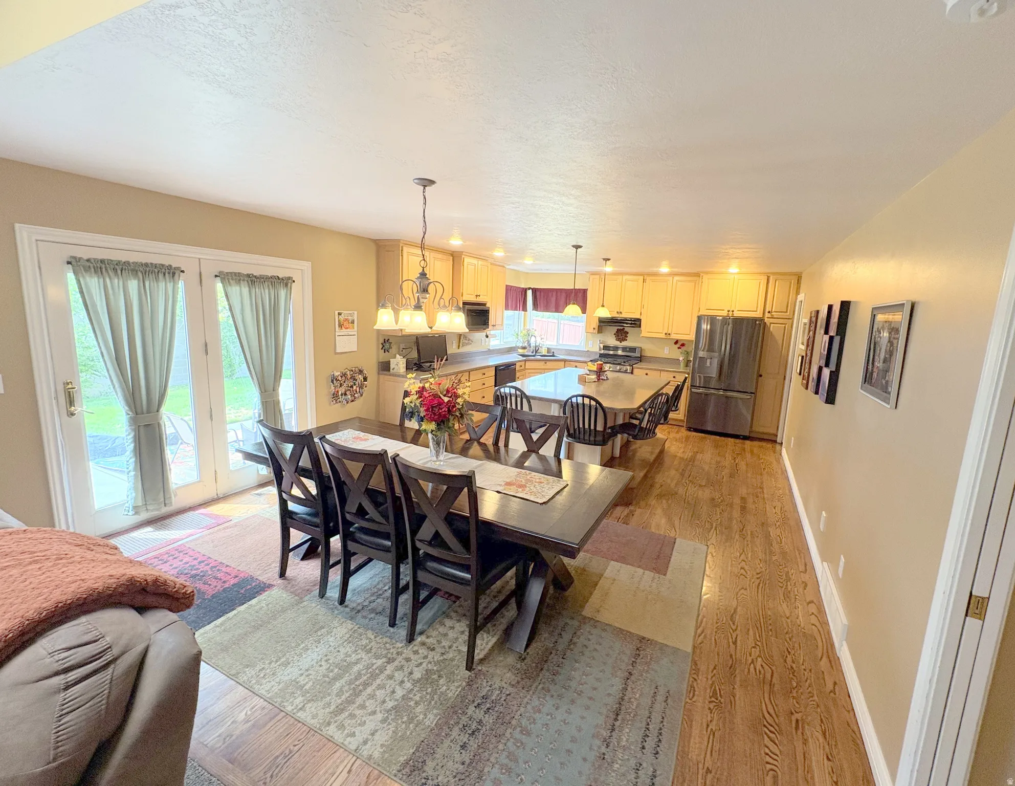 Open-concept kitchen and dining area featuring wood-finish flooring, light wood cabinetry, stainless steel refrigerator, and a kitchen island with seating
