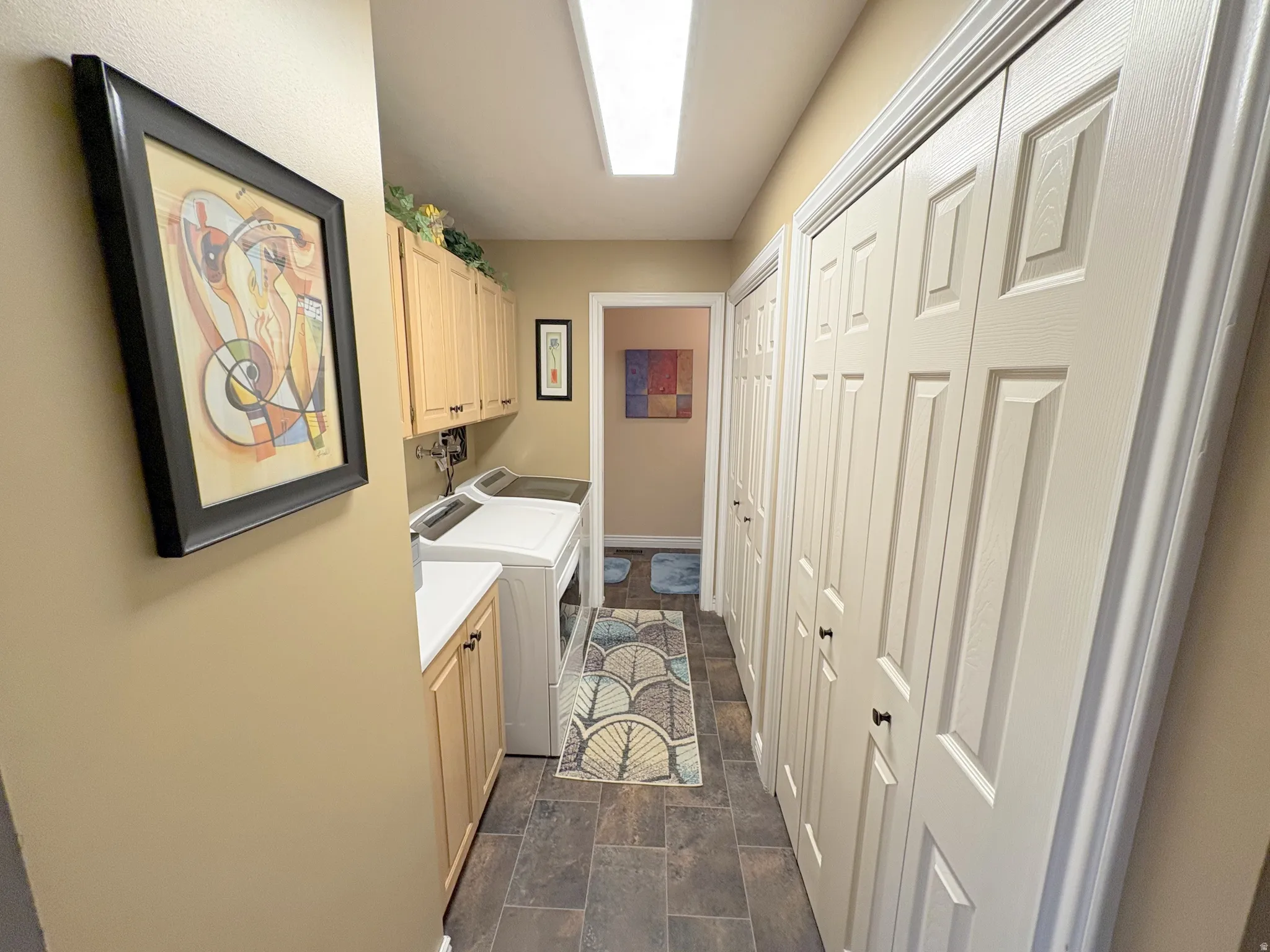 Laundry area featuring light wood-finish cabinetry, a white countertop, and dark tile flooring