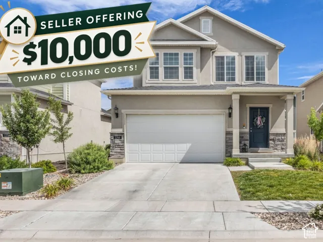 Two-story stucco exterior featuring stone veneer accents, multi-pane windows, covered entryway, and a concrete driveway