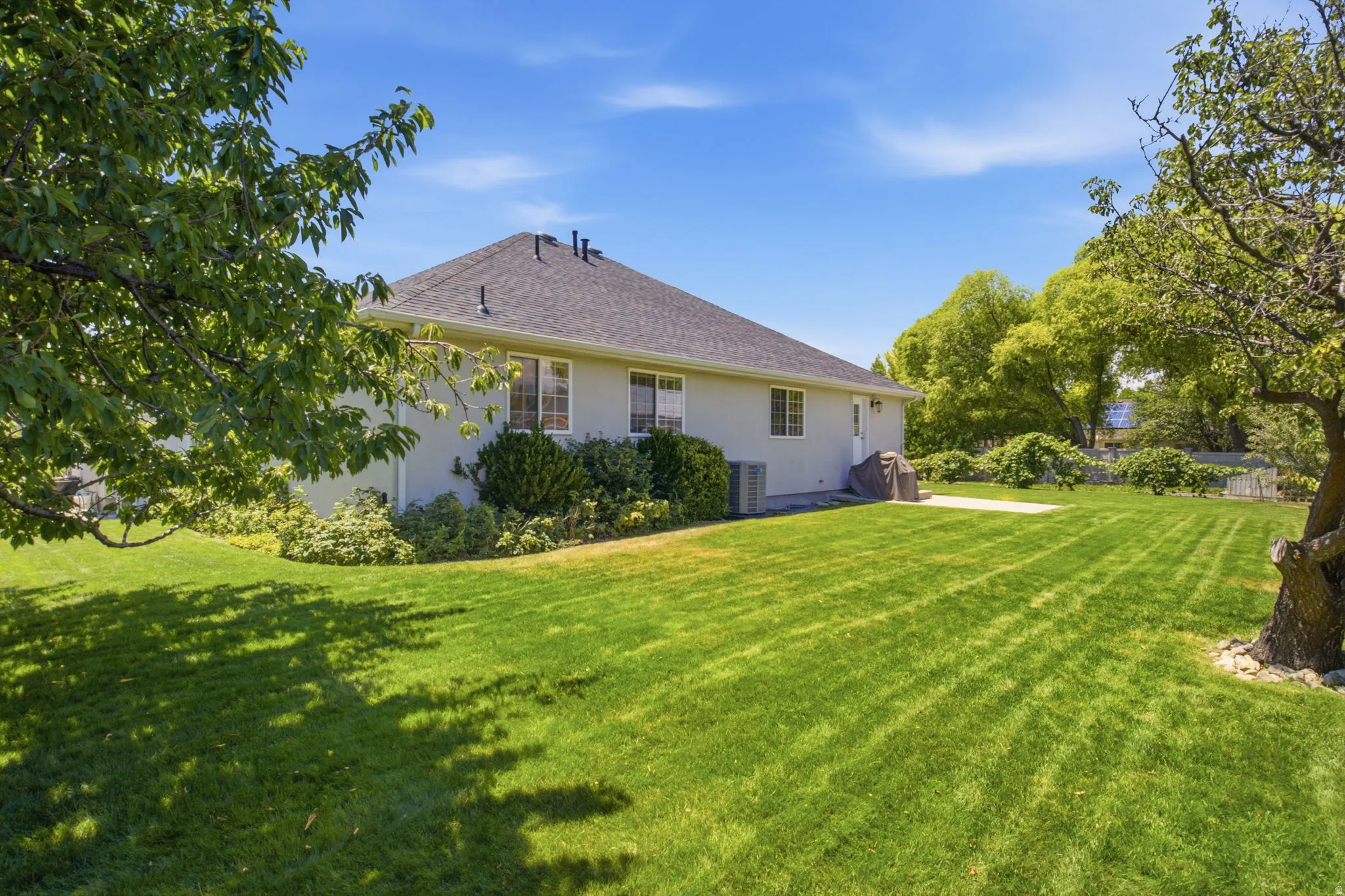 Expansive rear yard featuring a large green lawn, mature trees, and a concrete patio