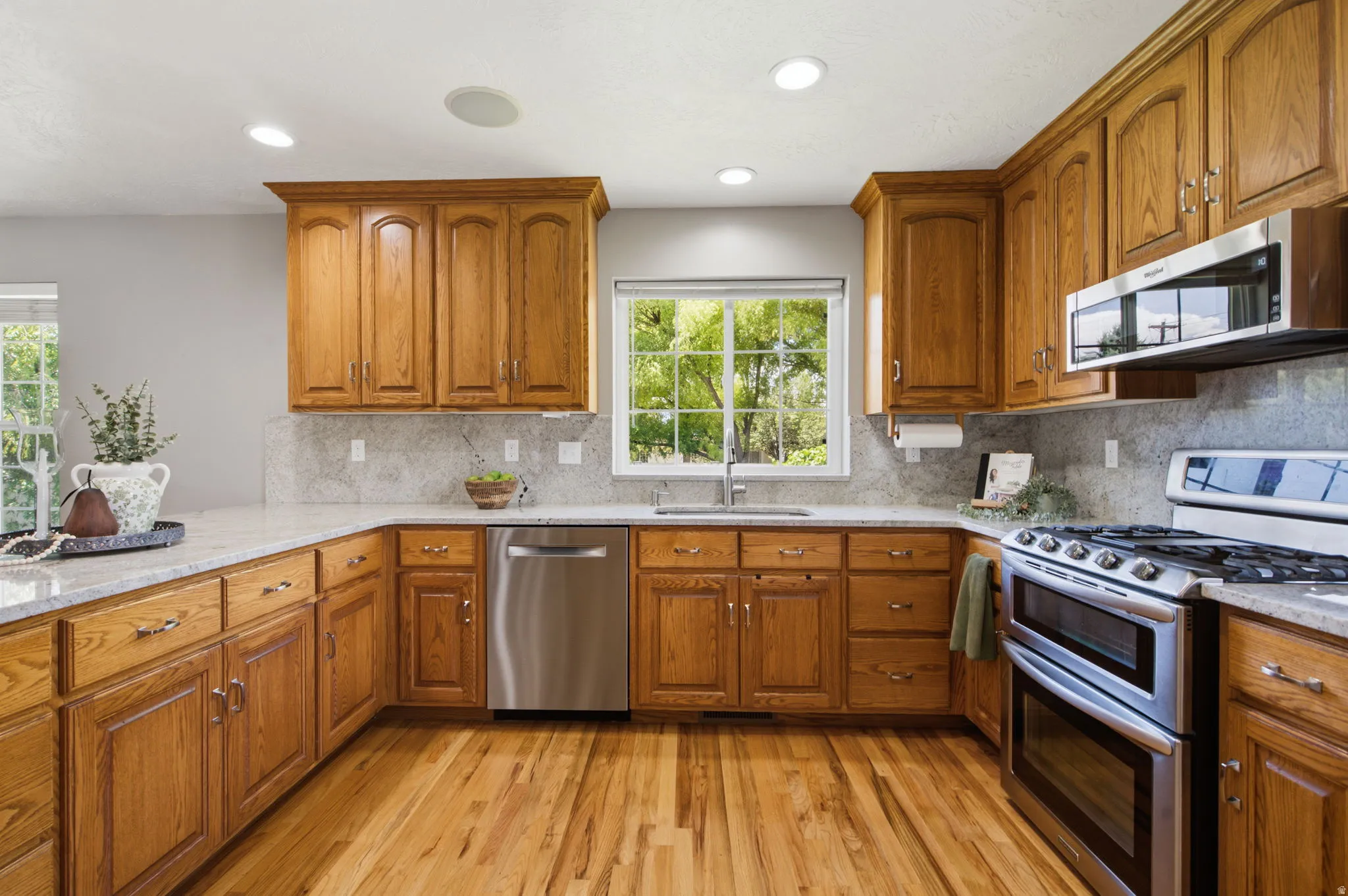 Kitchen featuring wood cabinetry, stainless steel appliances, light-toned countertops, tile backsplash, and wood-finish flooring