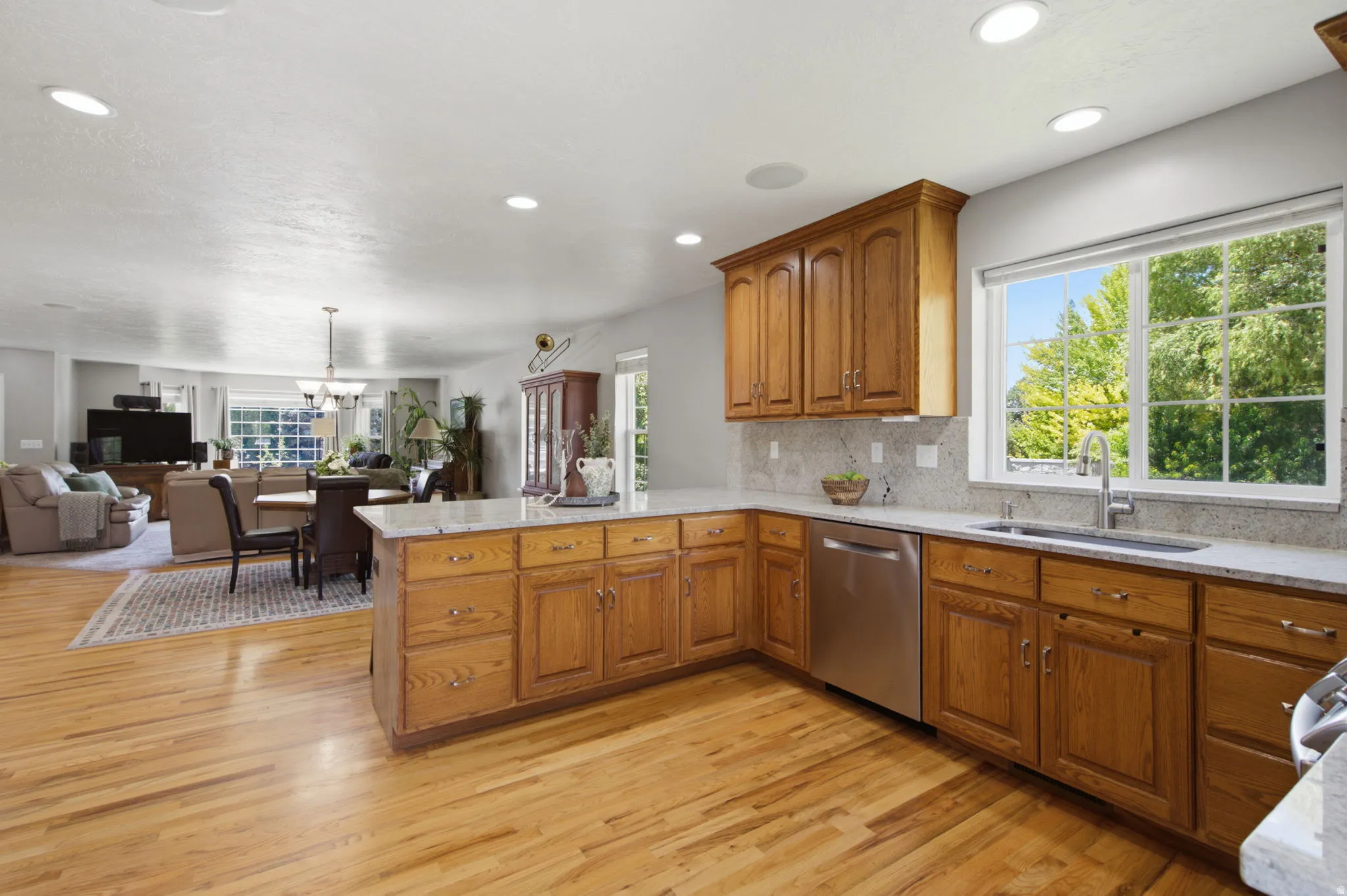 Kitchen featuring wood-finish cabinetry, light-toned countertops, stainless steel appliances, a window above the sink, and recessed lighting