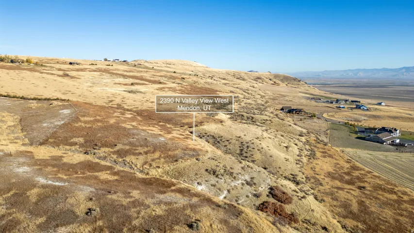 Expansive sloping terrain featuring natural vegetation, distant mountain range, and scattered residential properties
