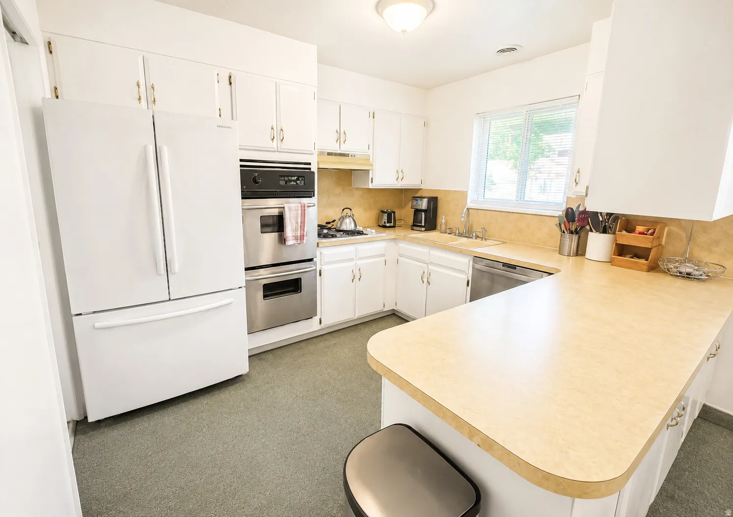 Kitchen featuring extensive white cabinetry, integrated stainless steel double ovens, a built-in cooktop, light-toned countertops, and a window above the sink