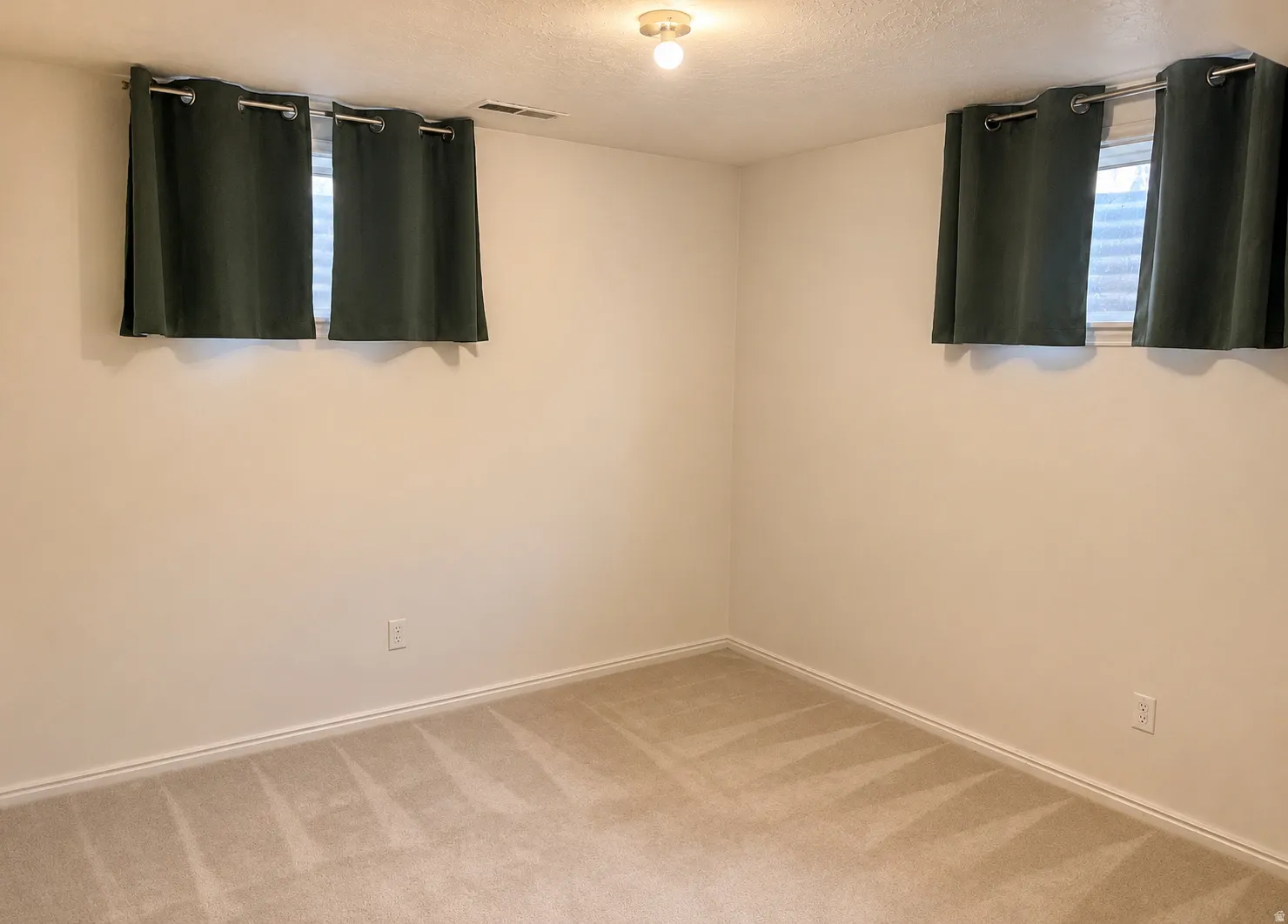 Carpeted room with neutral wall tones and two windows featuring  drapery
