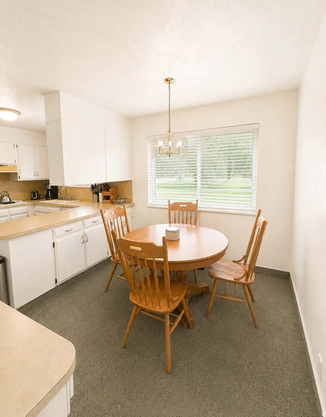 Kitchen eating area with a large window, brass chandelier, and light-colored countertops