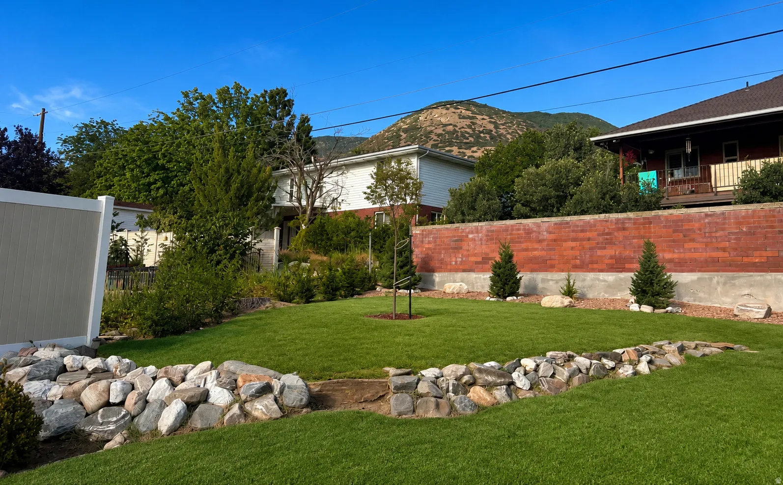 Expansive green lawn with a rock-lined border, bordered by a brick wall and various plantings