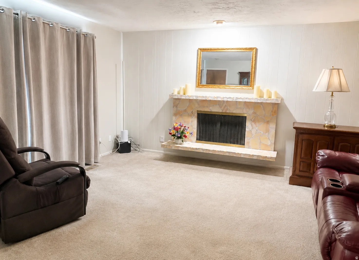 Living area featuring a stone-clad fireplace, paneled accent wall, and neutral carpet flooring