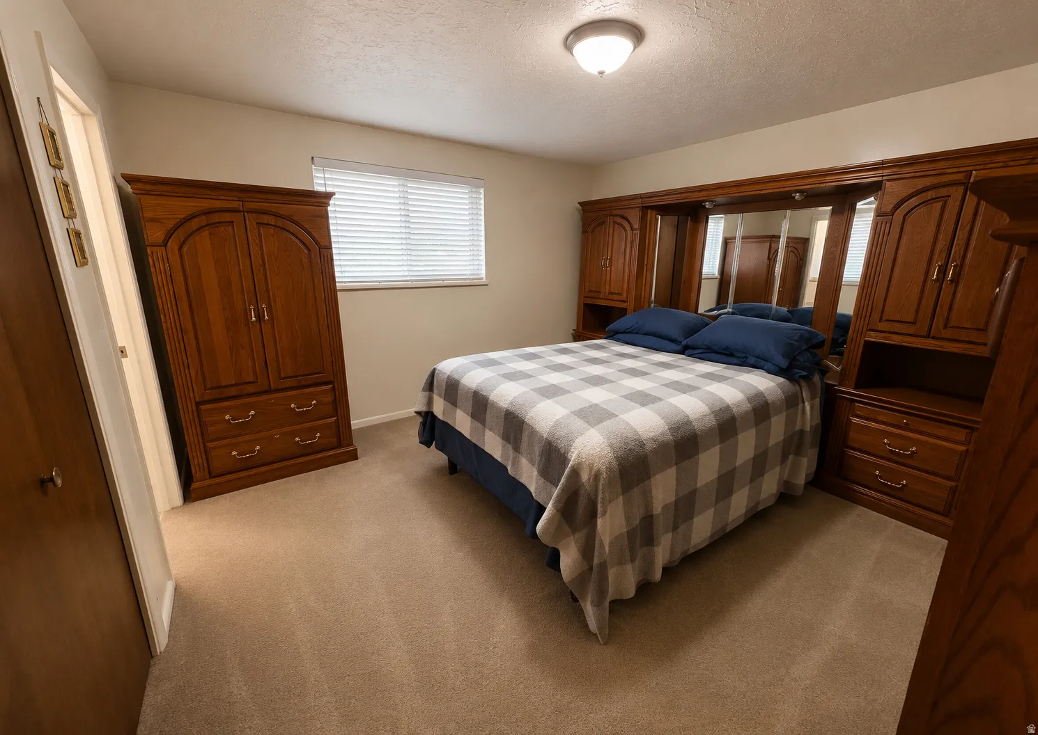 Bedroom featuring light beige carpeting, a window with horizontal blinds, and a built-in wooden wardrobe unit with mirrored panels