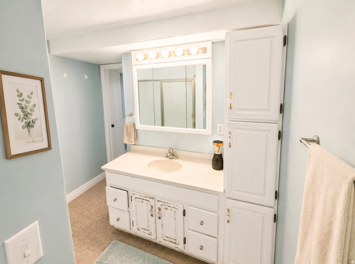 Bathroom featuring a white vanity with integrated sink, a medicine cabinet with mirror and overhead lighting, and a tall built-in storage cabinet
