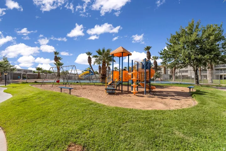 Outdoor playground area featuring a multi-level play structure with slides and climbing elements, a swing set, and a sand base