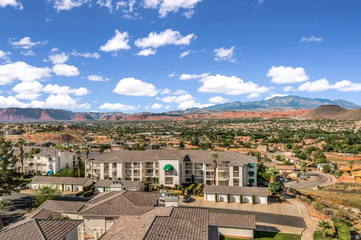 Expansive desert and mountain scenery frames a multi-story residential building featuring multiple balconies and green awnings