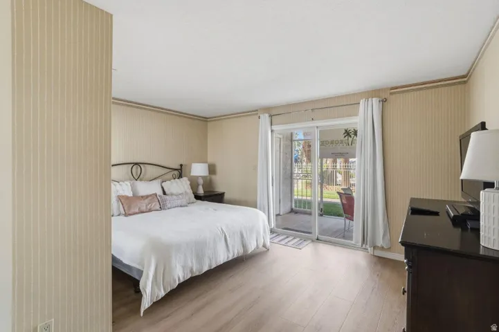 Bedroom featuring wood-finish flooring, patterned wallpaper, a sliding glass door to an outdoor patio, and a privacy wall