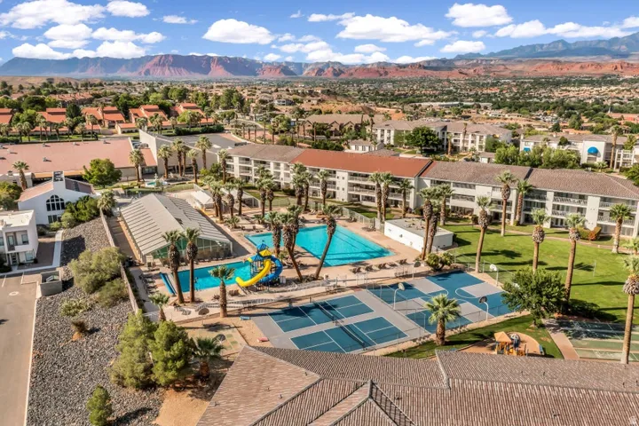 Community recreation area featuring multiple swimming pools, a covered pool structure, sports courts, and mature palm trees