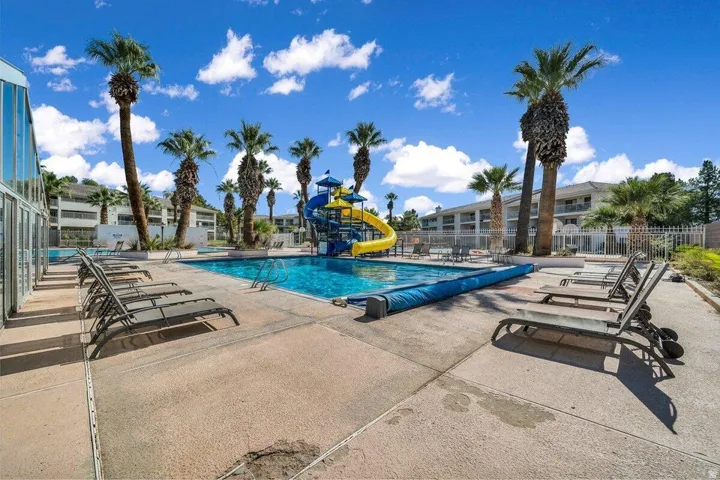 Expansive outdoor pool area featuring a large swimming pool with an attached water slide structure, surrounded by concrete decking and numerous palm trees