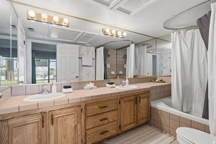 Bathroom featuring a dual vanity with tile countertop, wood cabinetry, and integrated sinks