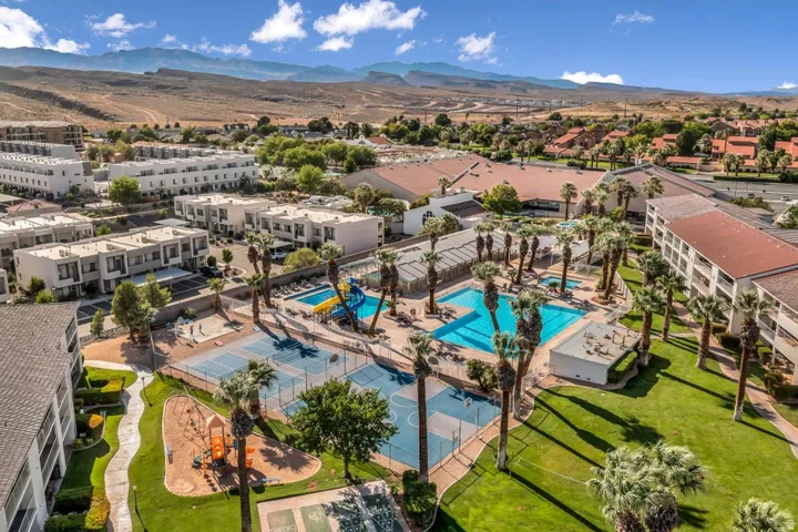 Expansive community amenities including multiple swimming pools, a water slide, tennis courts, and lush green spaces, all framed by distant mountain ranges