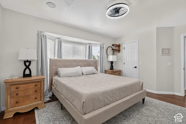 Bedroom featuring a bay window with blinds and drapes, a tufted upholstered bed frame, and wood-finish flooring