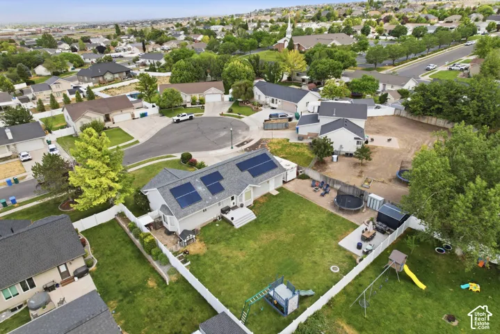 White-sided residence with solar panels on a gray shingled roof, featuring a fenced backyard with a manicured lawn and mature trees
