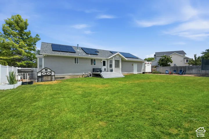 Expansive rear yard featuring a large lawn, privacy fencing, and a multi-panel solar energy system on the roof