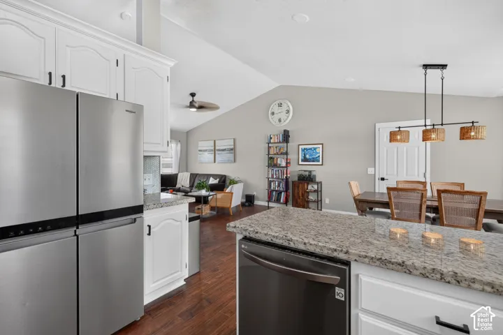 Open concept kitchen with wood-finish flooring, white cabinetry, stainless steel refrigerator, and stone countertops