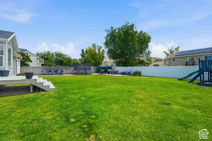 Expansive green lawn featuring a multi-level deck with steps, a paved patio area, and a privacy fence