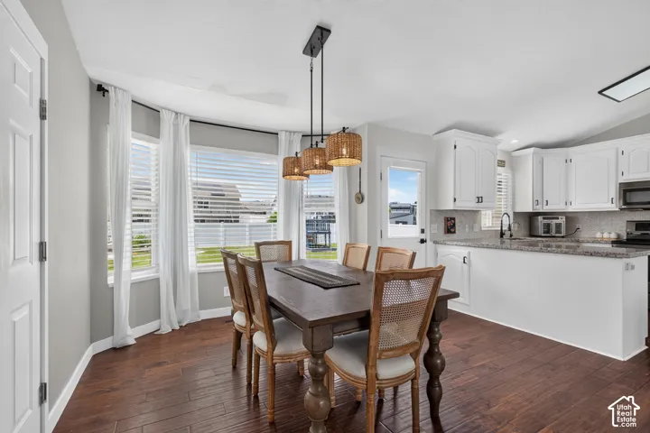 Open-concept dining area featuring wood-finish flooring, a bay window with blinds, and a multi-pendant light fixture